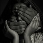 A person with hands covering their eyes and mouth in a black and white portrait
