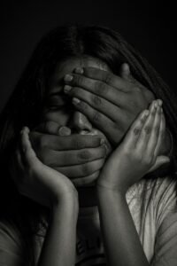 A person with hands covering their eyes and mouth in a black and white portrait