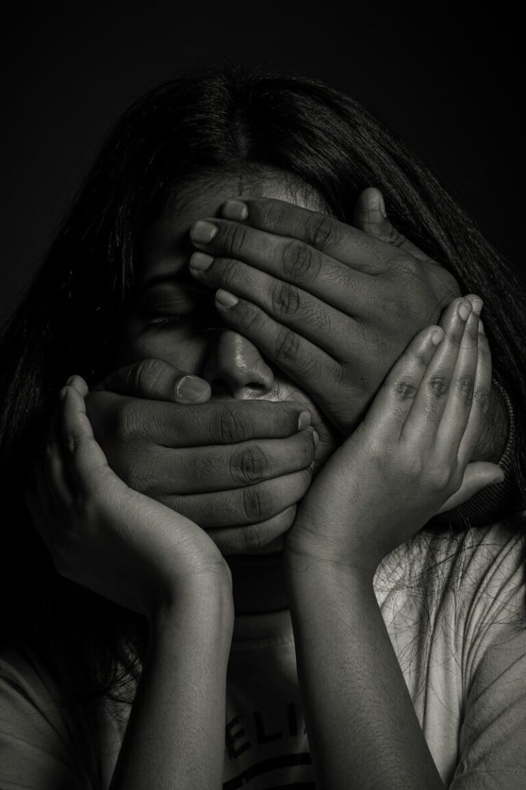 A person with hands covering their eyes and mouth in a black and white portrait