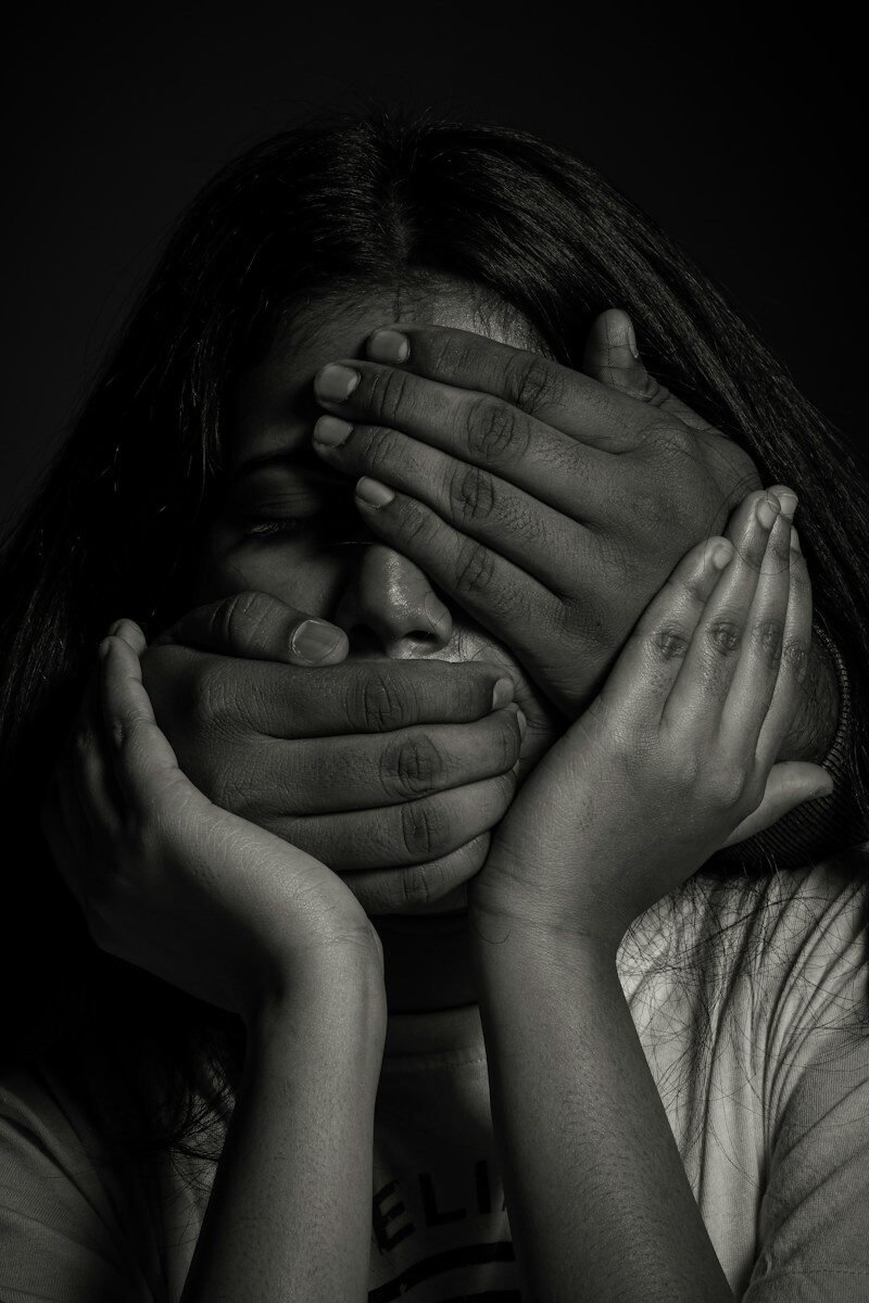 A person with hands covering their eyes and mouth in a black and white portrait